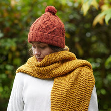 Woman wearing rust orange handmade wool bobble hat styled with chunky mustard yellow knitted scarf outdoors