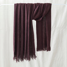 Plum purple banana yarn scarf with fringe detailing draped on a white clothing rack against a neutral background.