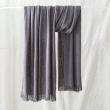 Soft grey woven winter scarf with fringe edges displayed hanging against a neutral background.