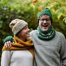 Man wearing forest green wool bobble hat and fair isle neckwarmer beside woman in mustard scarf and knitted winter accessories outdoors