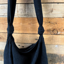 Close-up of black cotton crossbody shoulder bag with knotted handles and zipper closure against rustic wood background