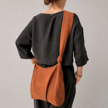Handmade rustic orange cotton shoulder bag with soft structure and knotted shoulder straps on neutral background