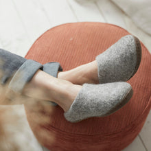 Woman wearing light grey wool mule slippers at home with felted wool uppers and suede soles.