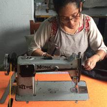 Artisan sewing handmade canvas bags using industrial sewing machine in ethical workshop setting.