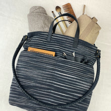 Black striped handmade tote bag styled with beige canvas pouch, makeup brushes and wooden comb.