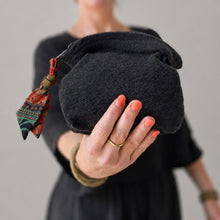 Handmade black cotton cosmetic pouch with colourful artisan zip pull held in hand against neutral background
