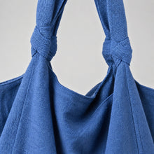 Close-up of a handmade blue cotton tote bag showing woven fabric texture and knotted strap details