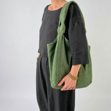 Model carrying an oversized ivy green cotton tote bag with knotted shoulder straps and soft slouchy design