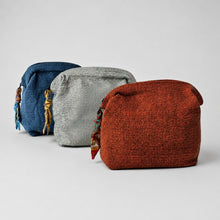 Handwoven cotton zip pouches in rust red, grey and blue arranged diagonally on a soft grey background.