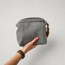 Hand holding handmade grey cotton makeup pouch with zip closure and artisan fabric pull detail