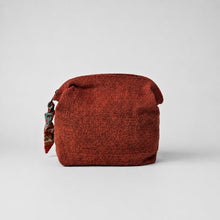 Rust red handwoven cotton zip pouch with patterned fabric zip pull on a soft neutral grey background.