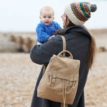 Woman carrying a beige cotton canvas backpack while holding a baby outdoors in a winter lifestyle setting.