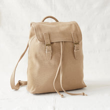 Front view of a beige cotton canvas backpack with brass buckle straps and drawstring closure.