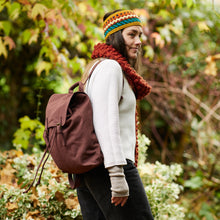 Side profile of woman wearing a brown cotton canvas backpack while walking outdoors in autumn scenery.