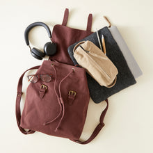 Flat lay of a brown cotton canvas backpack with headphones, laptop sleeve, pencil pouch and everyday essentials.