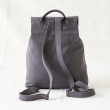 Rear view of a grey cotton canvas backpack showing adjustable shoulder straps and top carry handle.