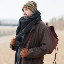 Man wearing a brown cotton canvas backpack with winter clothing and knit accessories in an outdoor landscape.