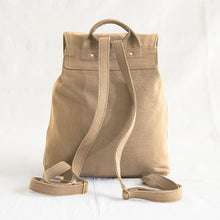Rear view of a minimalist beige cotton canvas backpack with adjustable shoulder straps and top carry handle.