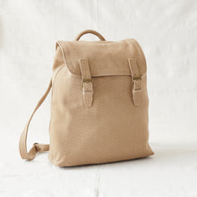 Minimalist beige cotton canvas backpack with flap closure and adjustable shoulder strap against neutral background.