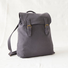 Front view of a minimalist grey cotton canvas backpack with brass buckle straps and adjustable shoulder strap.