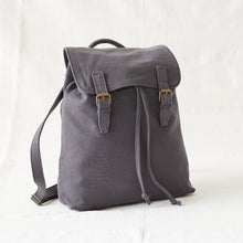 Grey cotton canvas backpack featuring flap closure, brass buckles and adjustable drawstring opening.