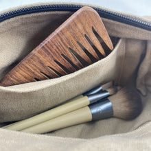Close-up of beige canvas pouch interior with wooden comb and makeup brushes inside storage compartment.