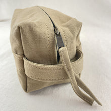 Close-up side detail of beige canvas toiletry pouch with durable stitching and zipper closure.