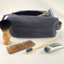 Grey canvas toiletry pouch styled with shaving brush, wooden comb, toothbrush and grooming essentials.
