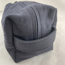 Close-up side view of grey canvas toiletry pouch with sturdy stitching and minimalist design.
