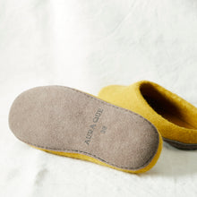 Close-up of mustard yellow felted wool slippers showing the AURA QUE suede sole and stitched finish.