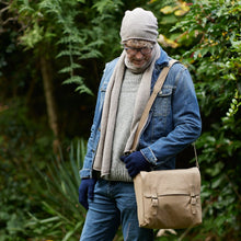Man wearing handmade beige canvas messenger bag outdoors with casual winter clothing and sustainable style.