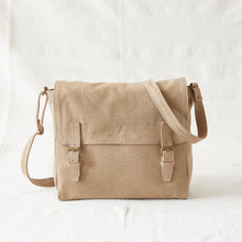 Front view of handmade beige canvas messenger bag with adjustable shoulder strap and brass buckle closures.