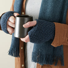 Close-up of blue chunky knit handwarmers and woven banana yarn scarf styled with a black ceramic mug.